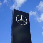 Elegant Mercedes Benz logo on a tall sign with a bright blue sky background.
