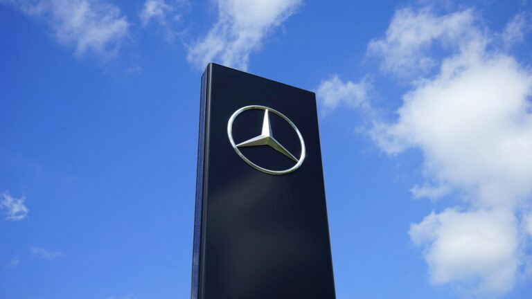 Elegant Mercedes Benz logo on a tall sign with a bright blue sky background.